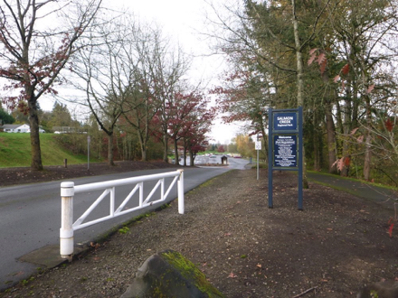Driveway into hard surface parking lot &ndash; hard surface sidewalk on the right &ndash; sign with information &ndash; parking fee booth