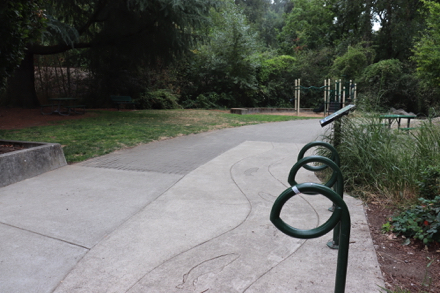Bike racks &ndash; two picnic tables, on pavement and under tree on natural surface &ndash; playground with bark-chip surface